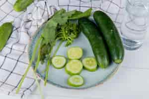 Free photo side view of vegetables as whole and sliced cucumber spinach coriander with cucumbers on cloth and detox water on wooden table