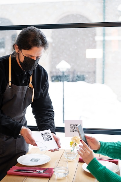 Free photo side view waiter with mask holding qr code