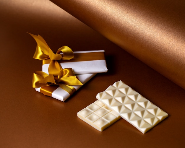 Free photo side view white chocolate bars with chocolate wrapped in white paper with gold ribbons