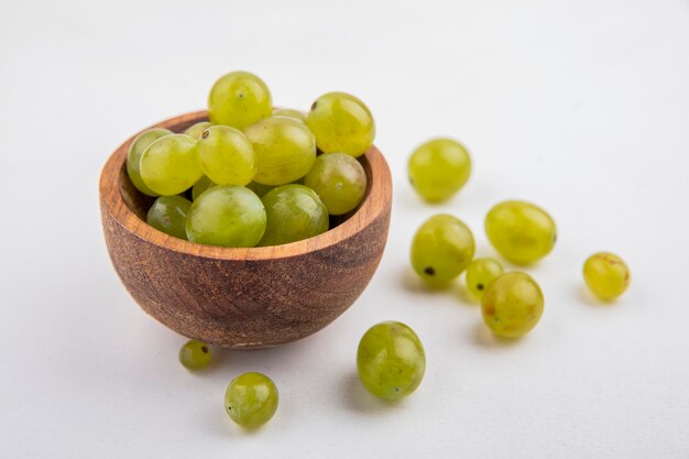 Side view of white grape berries in bowl and on white background