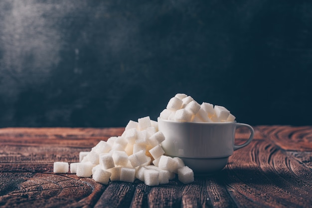 Free Photo side view white sugar cubes in a cup on dark and wooden table. horizontal