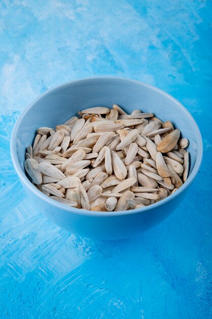 Side view white sunflower seeds with salt in the bowl on blue background