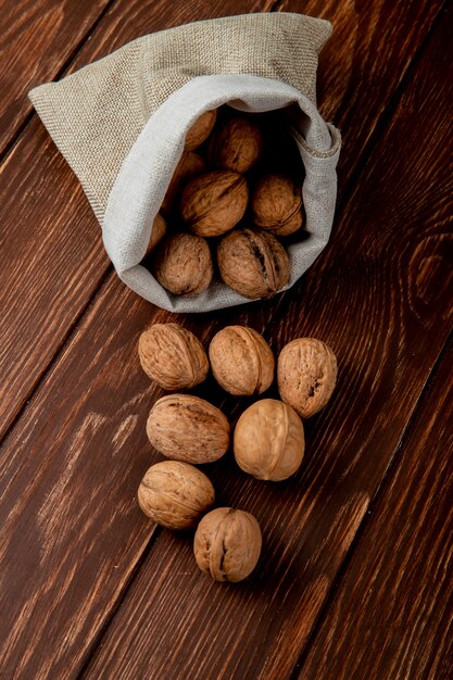 Side view of whole walnuts scattered from a sack on wooden background