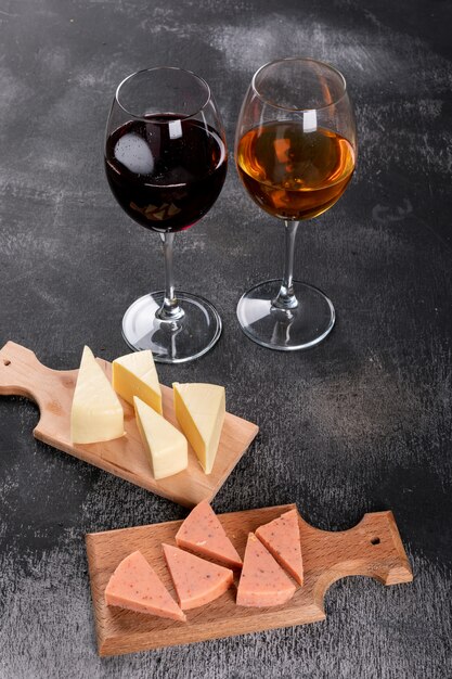 Side view of wine glasses and cheese on wooden cutting board on dark  vertical