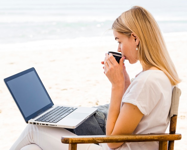 Free photo side view of woman at beach working and having coffee