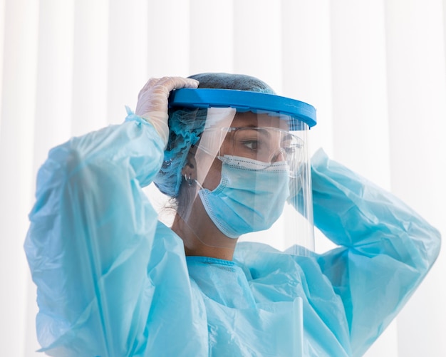 Free photo side view woman doctor putting on protective wear