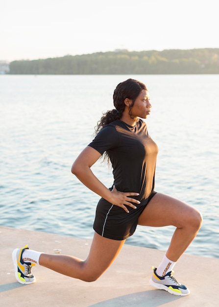 Free photo side view of woman doing lunges by the lake with copy space