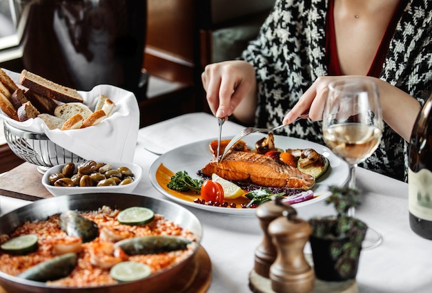 Side view of a woman eating baked salmon with vegetables at th table