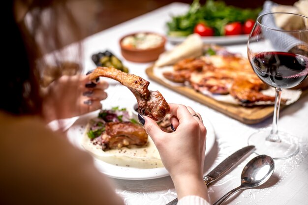 Side view woman eating kebab lamb rib with a glass of red wine