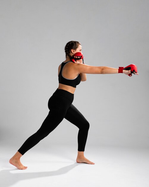 Side view woman in fitness clothes punching with box gloves