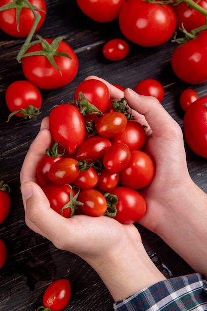 Side view of woman hands holding tomatoes with other ones on wooden surface