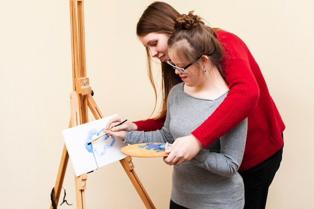 Side view of woman helping girl with down syndrome paint