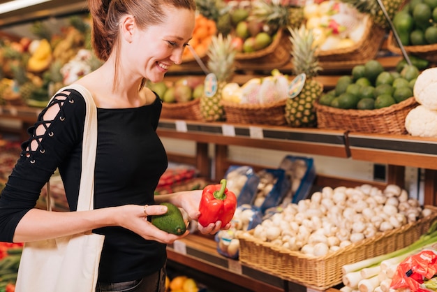 Free photo side view woman holding avocado and bell pepper