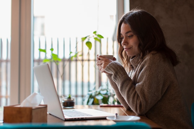 Side view of woman holding cup and looking at laptop