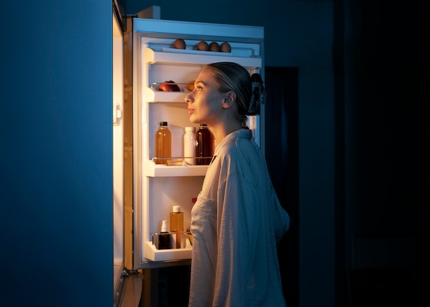 Free photo side view woman looking in the fridge