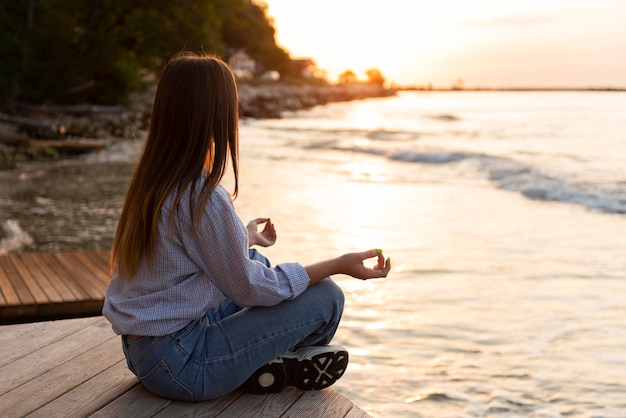 Free photo side view woman looking at the sea at sunset with copy space