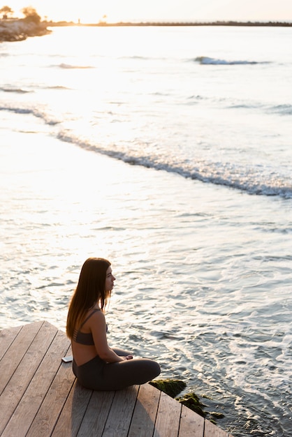 Free photo side view woman meditating next to the sea