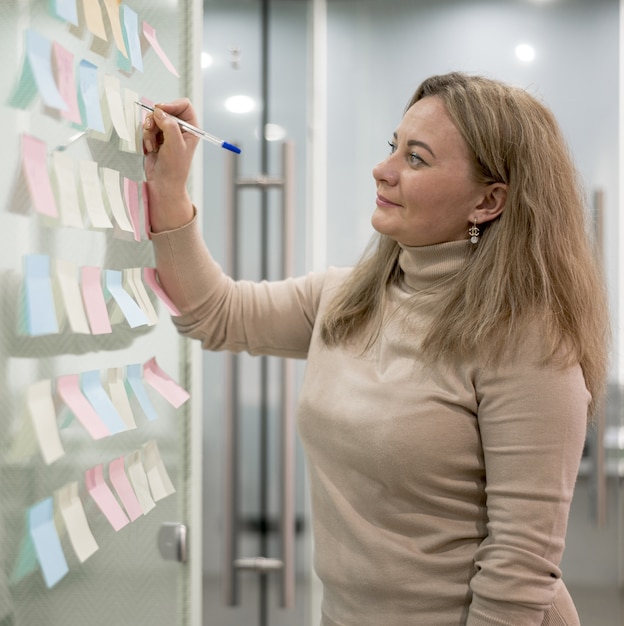 Free photo side view of woman in office writing on sticky notes