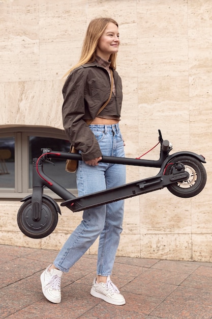 Free photo side view of woman outdoors holding electric scooter