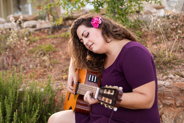 Side view of woman playing guitar with flower in hair