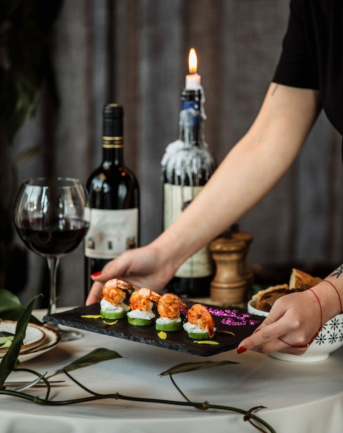 Free Photo side view of a woman putting a board with fried shrimps on grilled avocado topped with cream sauce