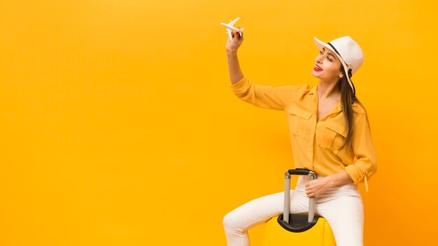 Free photo side view of woman sitting on luggage and holding plane figurine with copy space