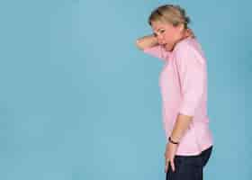 Free photo side view of a woman suffering from neck pain against blue wallpaper