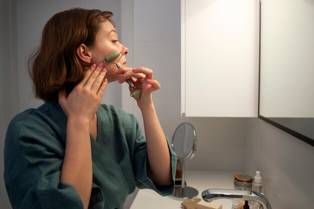 Side view woman using face roller for massage