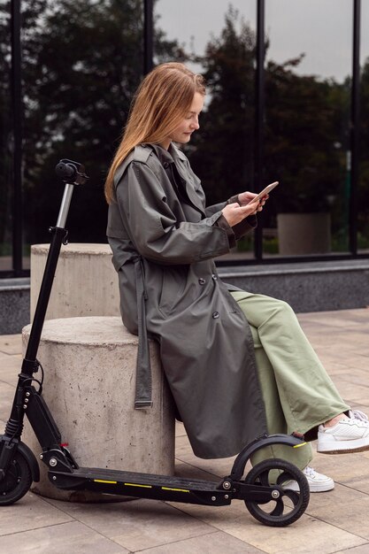 Side view of woman using her smartphone next to electric scooter