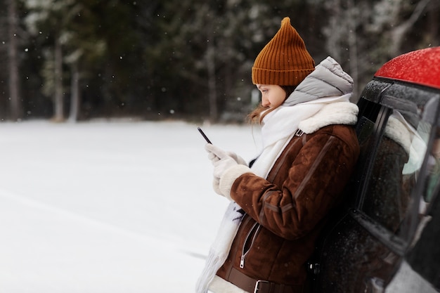 Free Photo side view of woman using smartphone next to car during a winter road trip