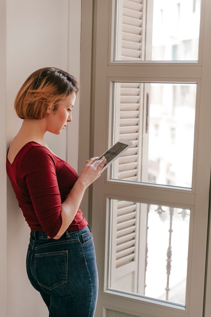 Free Photo side view woman using tablet near window