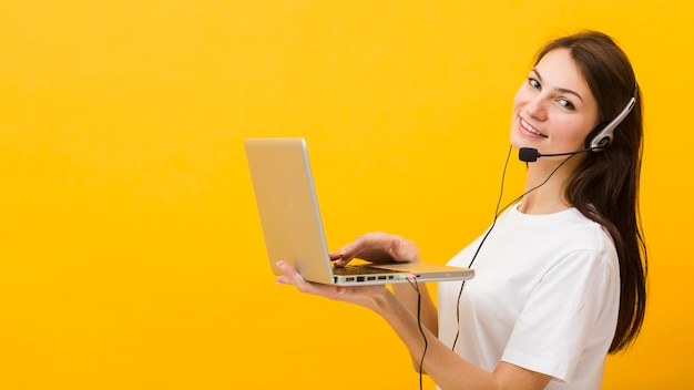 Free Photo side view of woman wearing headset smiling and holding up laptop