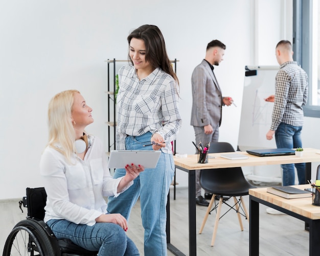 Free Photo side view of woman in wheelchair conversing with female colleague at office