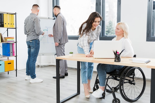 Free photo side view of woman in wheelchair conversing with female coworker at the office