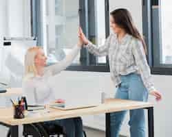 Free photo side view of woman in wheelchair at work high-fiving her colleague