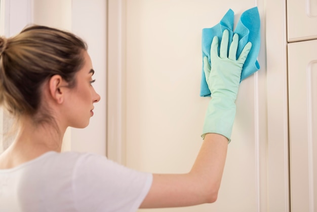 Side view of woman with glove cleaning surface with cloth