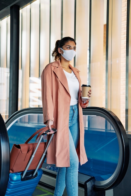 Side view of woman with luggage and medical mask during the pandemic at the airport