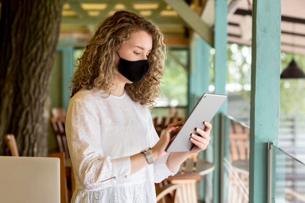 Free Photo side view woman with mask using tablet