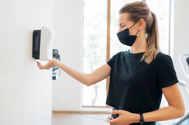 Free Photo side view of woman with medical mask disinfecting her hands at the gym