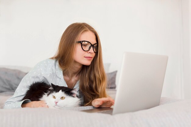 Free Photo side view of woman working on laptop from home in pajamas with cat