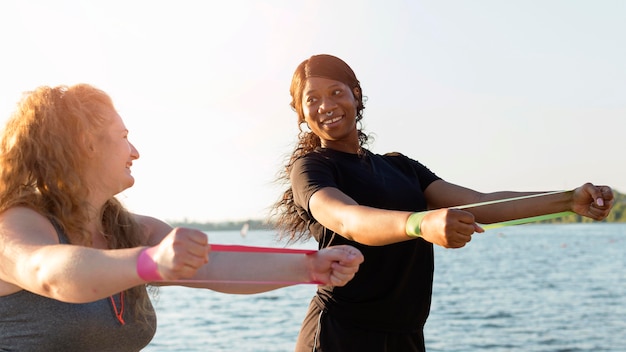 Free photo side view of women exercising with elastic bands by the lake