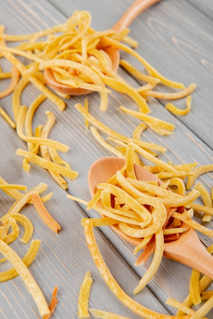 Free photo side view of wooden spoons with homemade italian raw pasta on wooden