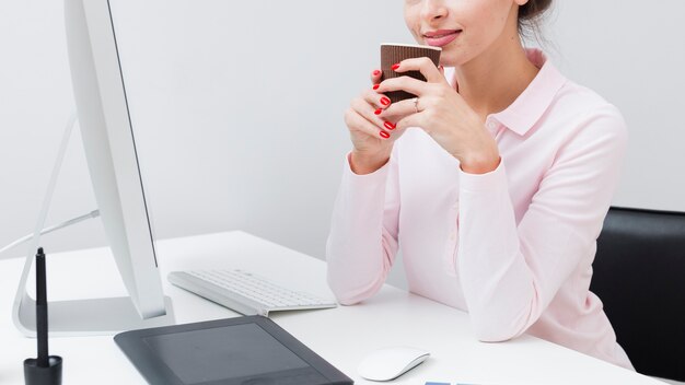 Side view of working woman at desk holding cup of coffee