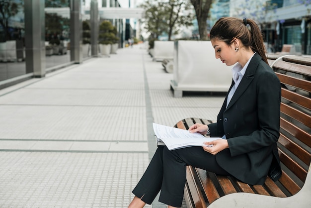 Side view of a young businesswoman sitting on bench reading the documents paper