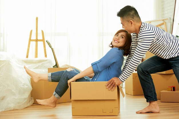 Side view of young couple having fun with package box in a room