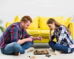 Free photo side view of young couple sitting on white carpet playing the chess game