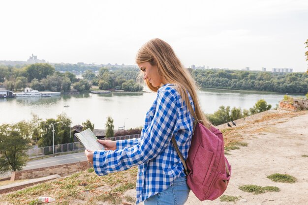 Side view of a young female hiker looking for direction in map