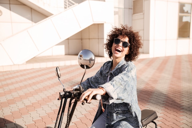 Side view of young joyful curly woman in sunglasses posing