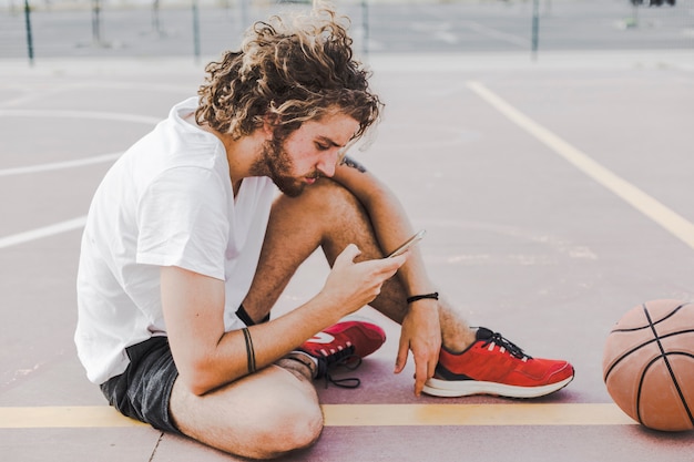 Free photo side view of a young male basketball player using smartphone