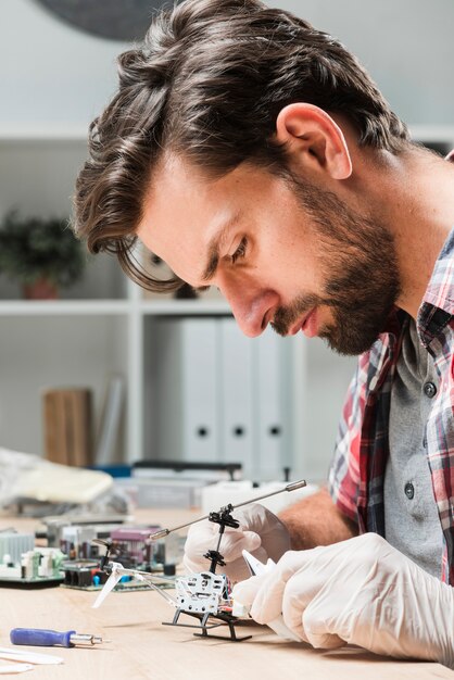 Free photo side view of young male technician repairing helicopter toy on wooden desk